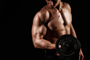 Muscular and fit young bodybuilder fitness male model posing over black background with DUMBBELL....