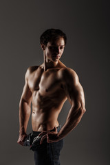 Fototapeta na wymiar Handsome athletic man looking side in unbuttoned jeans. Strong bodybuilder with six pack, perfect abs, shoulders, biceps, triceps and chest. Great fitness body. Ideal for commercial. Gray background