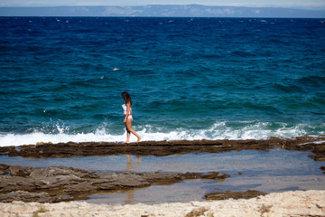 Woman in a white dres walks on the rocky beach 