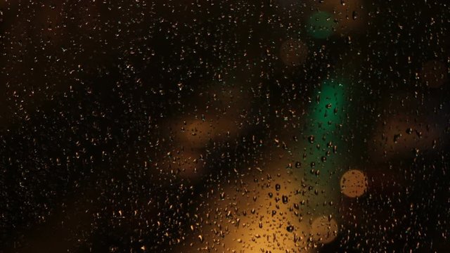 Luces de colores desenfocadas de letreros luminosos y de coches,  a traves de un cristal de ventana con gotas de lluvia y por la noche