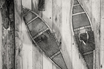 horizontal black and white image of a very old vintage pair of snowshoes hanging on a wall