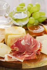 prosciutto with cheese and white wine in wooden board on brown background