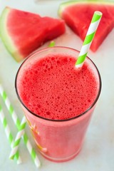 Watermelon juice in glass with striped straw and fruit slices on white marble background