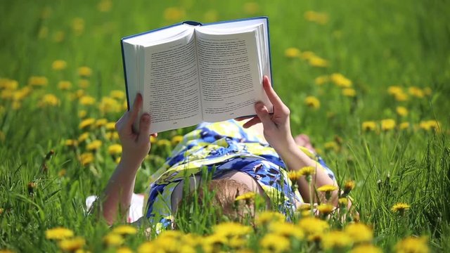 Girl reading a book sitting on a flower meadow with yellow dandelions
