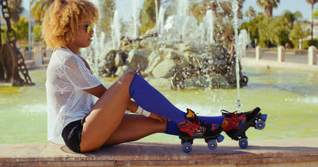 Slow Motion Video of Sexy Girl With Afro Haircut  She Adjusting Her Roller Skates While Sitting on Fountains Wall
