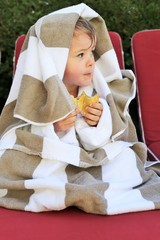 A young boy wearing a bathrobe and towels after exiting a swimming pool and enjoying a chocolate pastry.