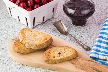 Three pieces of toast on a cutting board and glass bowl with cherry jam.