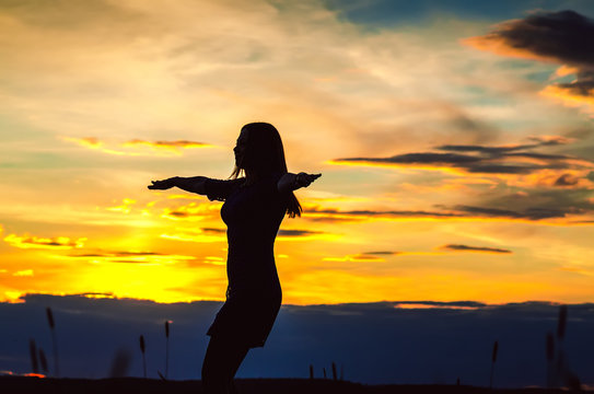 Healthy girl in a dress at sunset standing arms outstretched to the sides