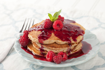 Whole wheat oatmeal pancakes with boysenberry sauce topped with red raspberries and a mint sprig - side view on a blue and white place mat