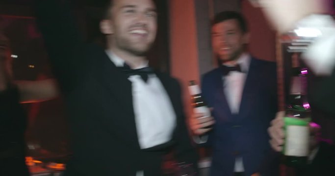 Handheld shot of friends dancing and singing with champagne bottles at party. Suitable for events, youth culture, entertainment, social gatherings, festive content