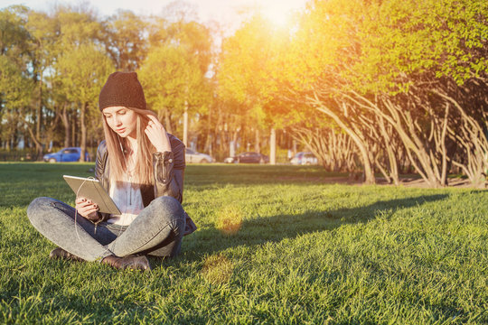 Young Student Woman Hipster Style sitting outdoor with tablet pc, listening music and communicate with friends through social network