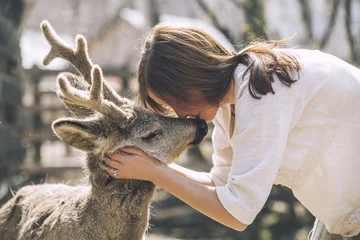 Foto op Plexiglas Ree Mooie jongedame knuffelen dierlijke reeën in de zon
