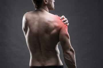 Pain in the shoulder. Muscular male body. Handsome bodybuilder posing on gray background