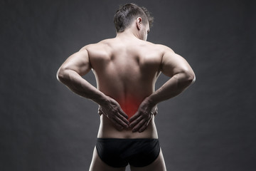Kidney pain. Man with backache. Handsome muscular bodybuilder posing on gray background. Low key close up studio shot