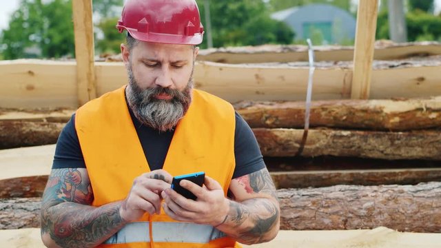 Serious worker or a construction worker sitting on the logs and writing sms