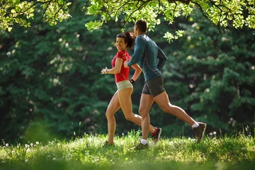 Gordijnen Jong koppel joggen in het bos. Groene omgeving. © BalanceFormCreative