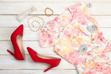 red shoes and dress with the beads with the bracelet and perfume on white wooden background