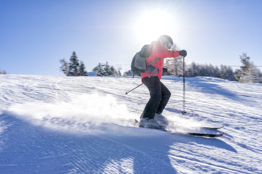 Female skier dressed in red jacket enjoys slopes in Italy with sun behind her.
