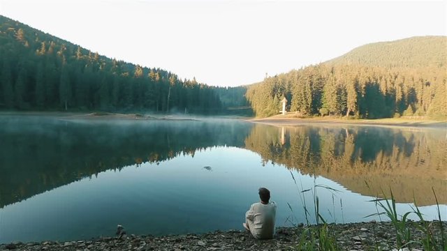 Handsome young thoughtful man in embroidery shirt throwing stones into the water and looking on the picturesque mountain lake Synevir. Ukrainian mythology concept