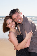 Fototapeta na wymiar Loving couple cuddling at the beach, look at the camera