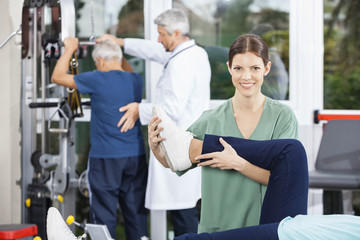 Physiotherapist Helping Patient With Leg Exercise In Fitness Cen