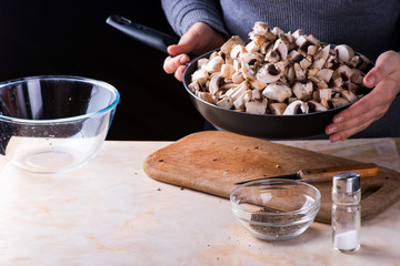 female hands hold fresh mushrooms in the pan