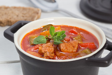 Gulasch in einer schwarzen cocotte mit Majoran auf weißem Holz