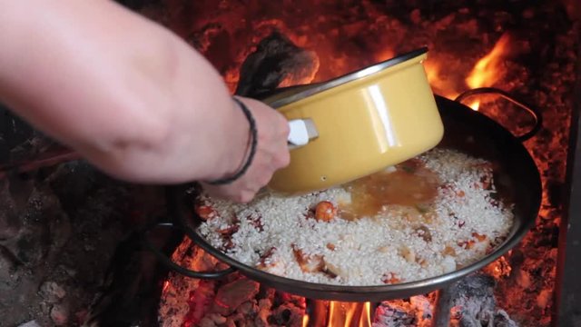Echando Caldo a la Paella de Marisco al Fuego de la  Chimenea para Cocer el Arroz