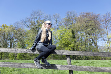 Obraz premium young blond girl with sunglasses on fence befrore fresh green sp