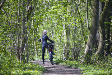 Obraz premium young blond girl with bicycle amongst fresh green spring foliage