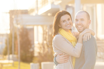 Young happy couple man and woman hug and look at the camera and smile sunbeam lens flare on background of sunset strong back light