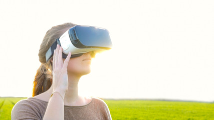 girl with virtual reality glasses standing in front of the sun in the nature