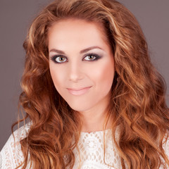 Smiling beautiful girl looking at camera in room. Attractive woman over gray.