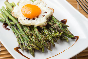 Asparagi verdi con uovo al tegamino su un piatto in ceramica bianco  ambientato