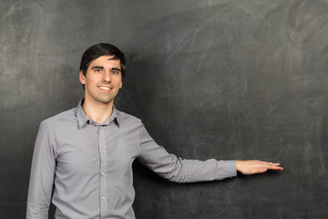 Portrait of young happy smiling teacher man standing near chalkboard background and showing something on it