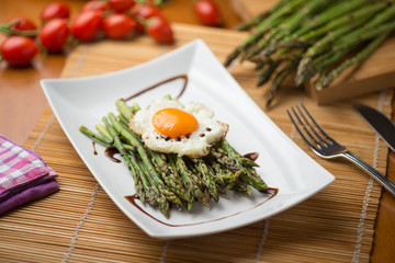 Asparagi verdi con uovo al tegamino su un piatto in ceramica bianco  ambientato