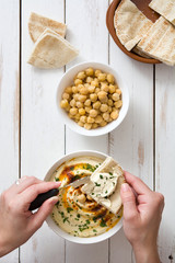 woman dipping hummus with pita bread on white wooden table