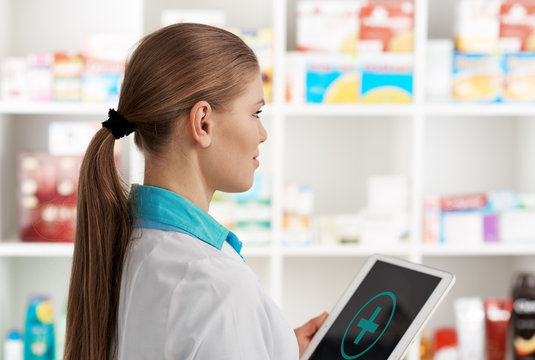 Young woman druggist holding digital tablet pc with cross symbol on the screen. Concept of medical aid and health care. 
