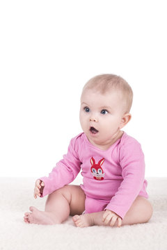 cute little baby in pink bodysuit sitting on a blanket and looking surprised to the side. adorable child girl with big blue eyes. happy family concept