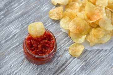 Potato chips with spicy tomato sauce on the wooden table