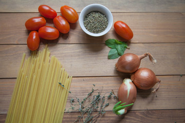 pasta, tomatoes, onions and spices on a wooden table
