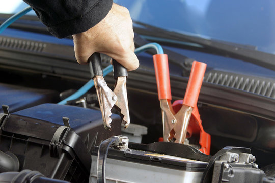 Hands installing battery booster cables on automotive battery