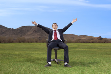 Businessman sitting on chair on green meadow