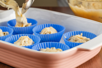 Woman hands cast dough for muffins.