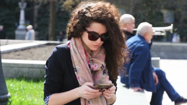 Young woman in sunglasses using smartphone outdoors