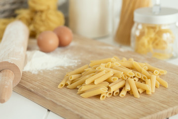uncooked dried penne over cutting board with flour and eggs
