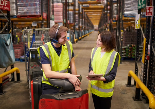Female warehouse manager and man on tow tractor discuss