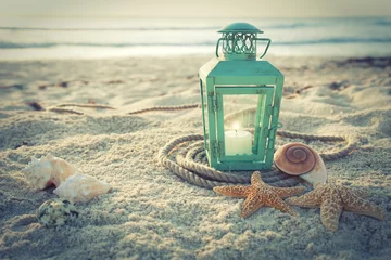Store enrouleur Plage et mer Lanterne traitée en croix sur la plage avec coquillages et corde au lever du soleil