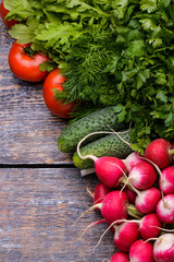 Spring vegetables and herbs in a basket: radishes, onions, parsley, cucumber on a wooden background.