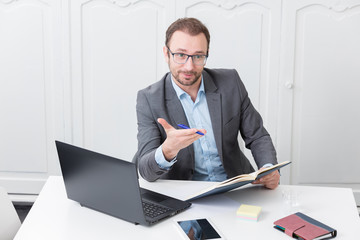 Businessman at the office desk gesticulates with a pen in his hand 